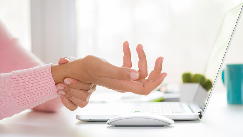 Woman holding wrist at computer