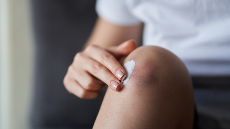 Woman putting lotion on knee 