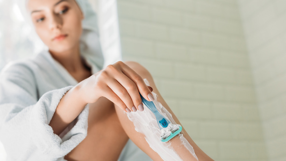 Woman shaving her legs with a blue razor 