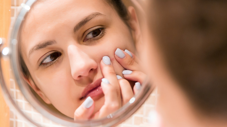 Girl squeezing pimple in mirror