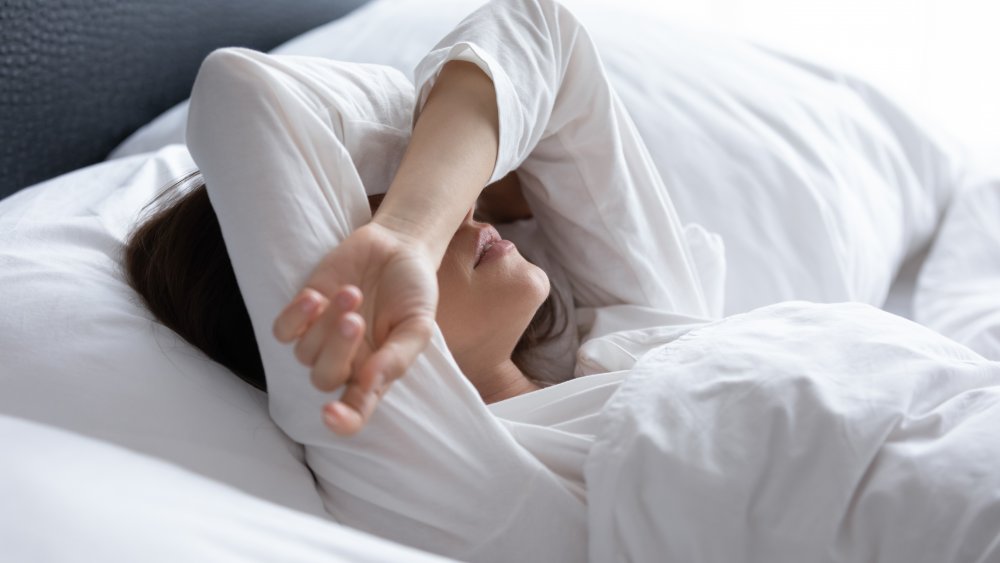 A woman in bed, with her arms over her eyes