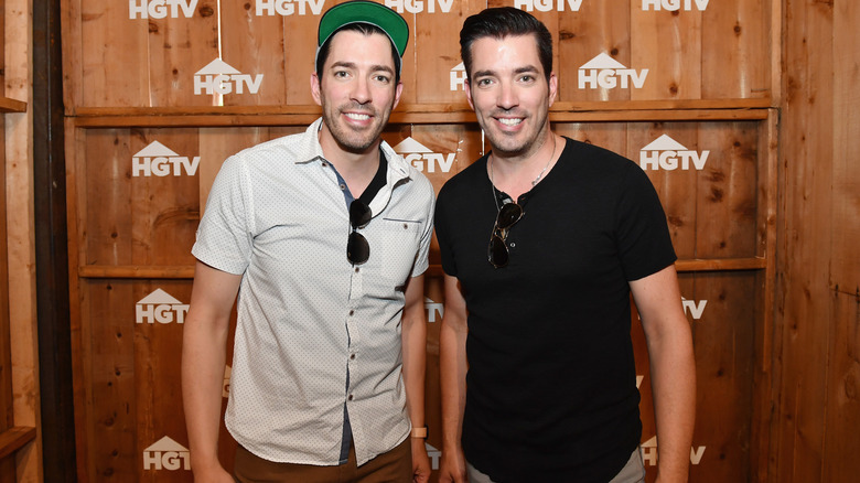 Drew Scott and Jonathan Scott standing in front of wooden HGTV backdrop