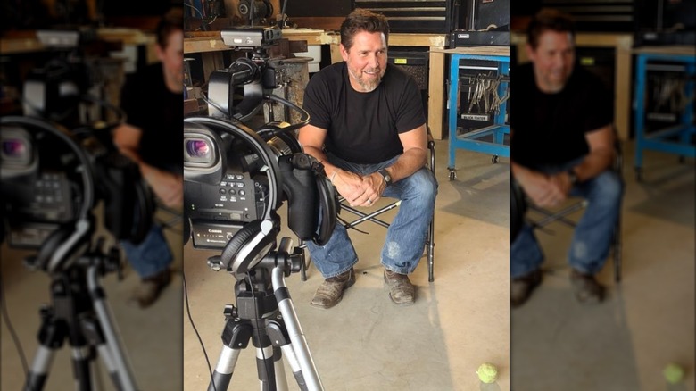 Tim McCellan prepares to film a clip for his show, sitting in a chair and smiling