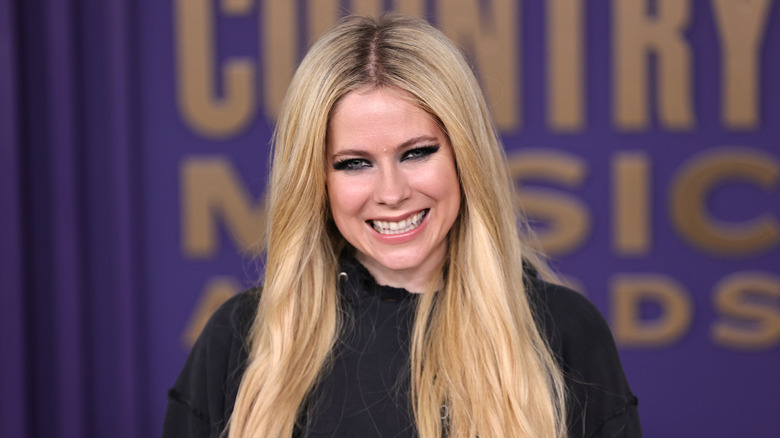Avril Lavigne smiling while posing at an event in a black outfit