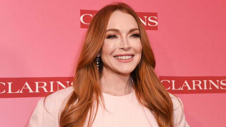 Lindsay Lohan smiling while posing at a Clarins event in a pink dress