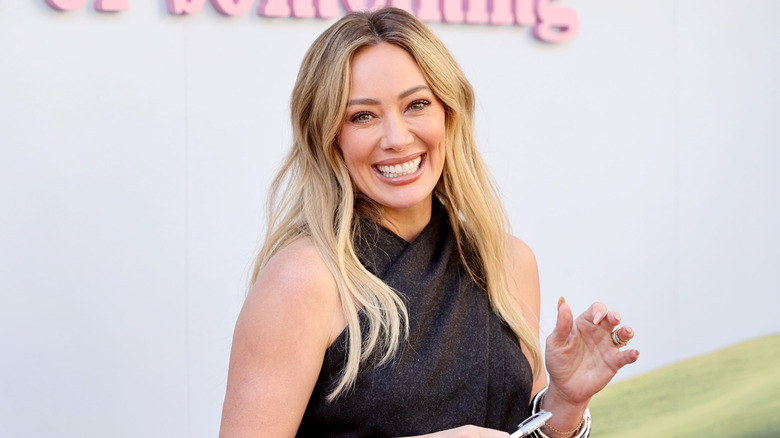 Hilary Duff smiling while posing with a pen in a black halterneck dress