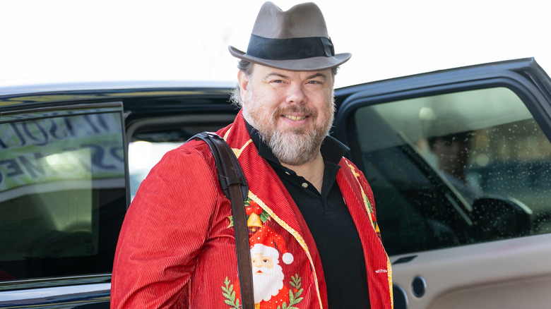 Devin Ratray smiling wearing Christmas outfit in front of car