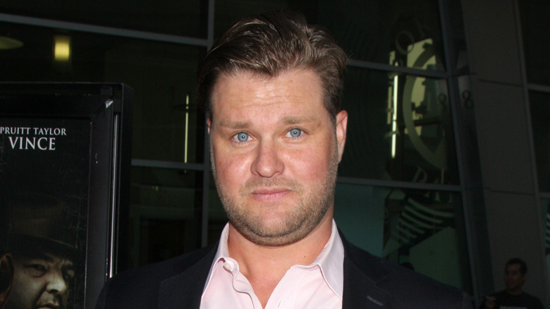 Zachery Ty Bryan grimacing while posing for photos in a black suit