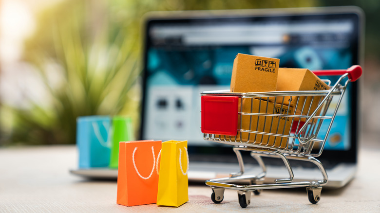 Miniature shopping cart with boxes in it in front of a laptop