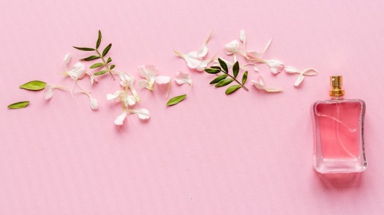 A perfume bottle spraying petals and leaves