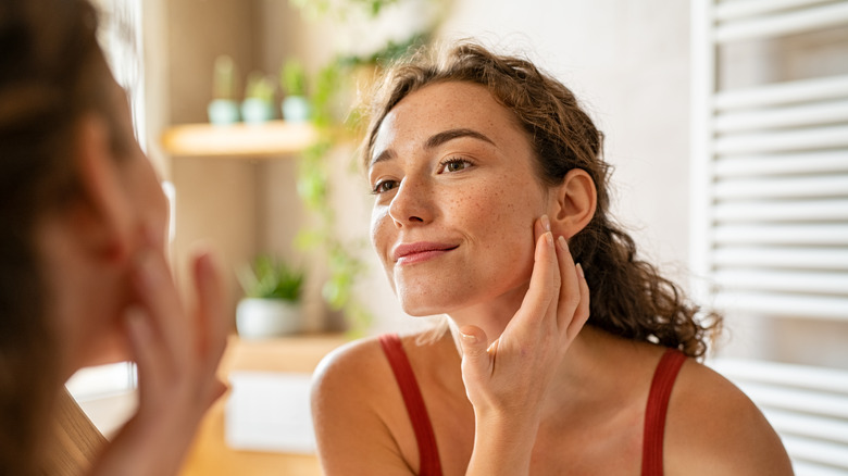 A woman applying skincare to her face and smiling 