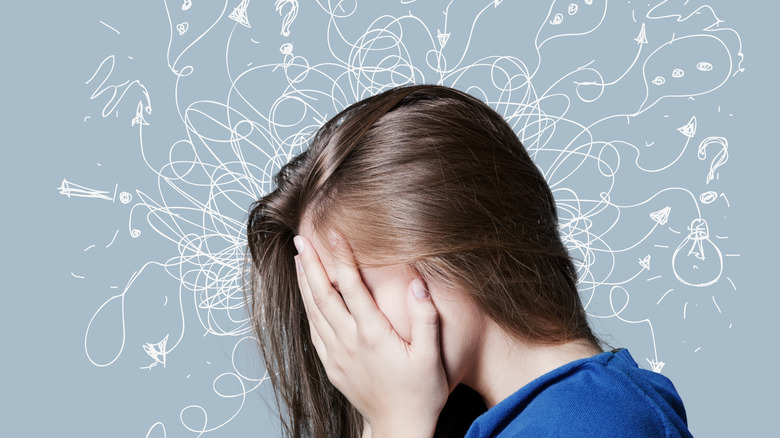 Brunette woman holding her face in front of a scribbled background representing ADHD.