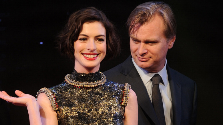 Anne Hathaway smiling and standing just in front of Christopher Nolan