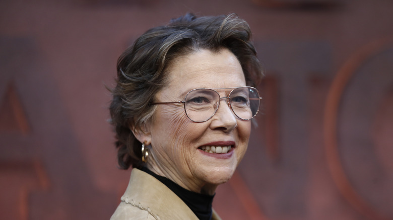 Annette Bening smiling in glasses and a tan jacket on the Dutton Ranch premiere red carpet