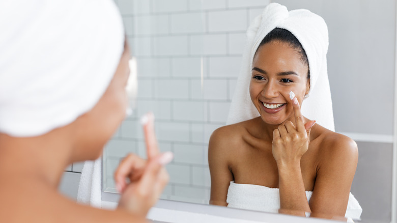 smiling woman applying face moisturizer