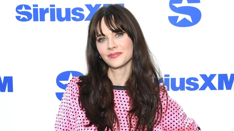 Zooey Deschanel smiling at SiriusXM in a pink dress with black polka dots
