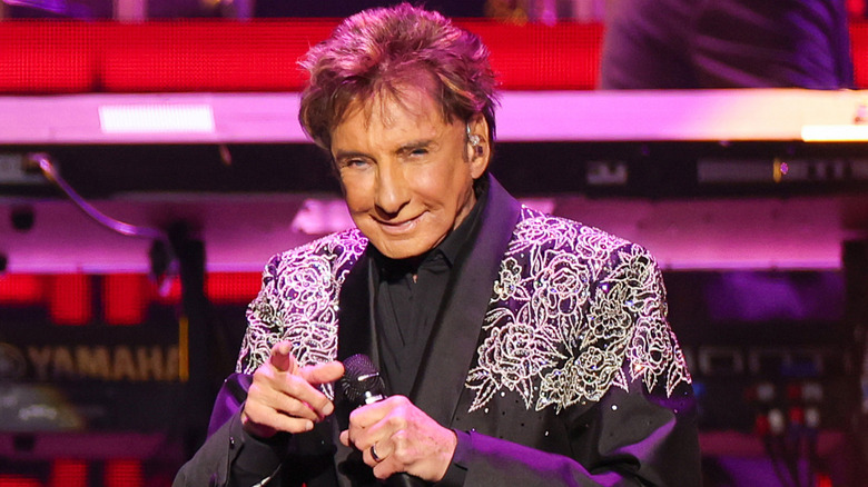 Barry Manilow in black appliqué jacket pointing at the camera while performing