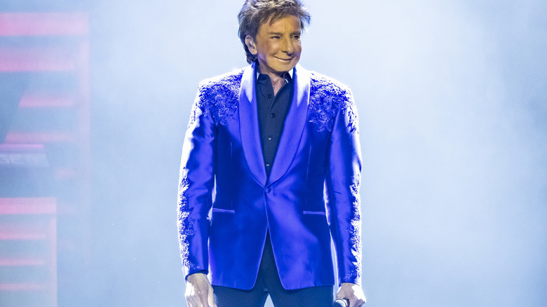 Barry Manilow smiling while standing on stage in a glitzy bright blue jacket