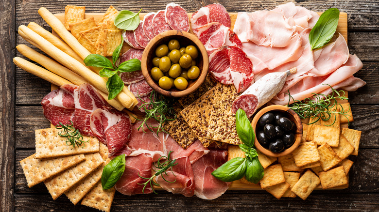 a charcuterie board featuring cured meats, olives, crackers and fresh herbs