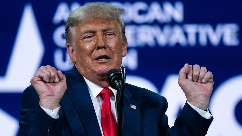 Donald Trump at CPAC with hands up in blue suit and red tie