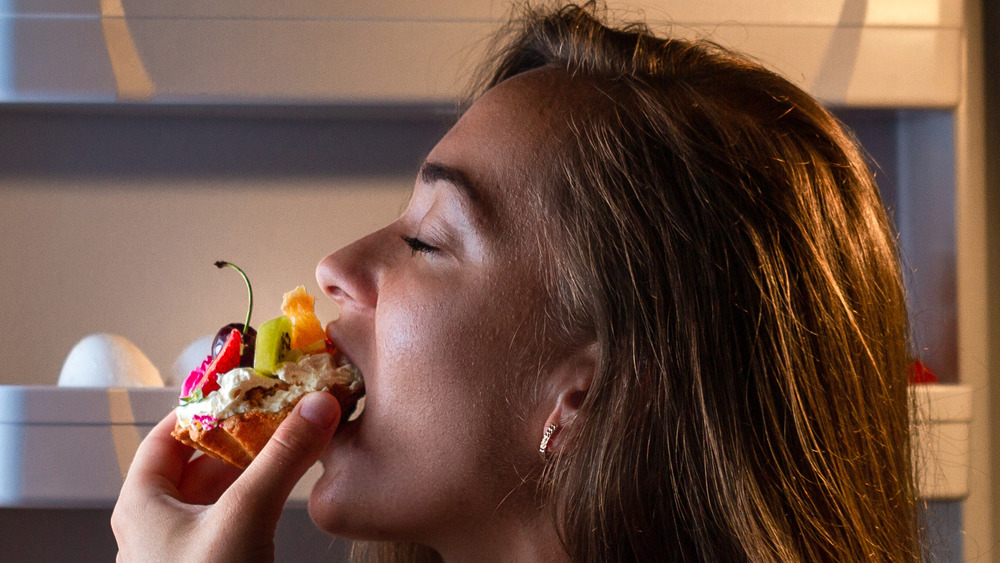 Young woman eating cake before bed 