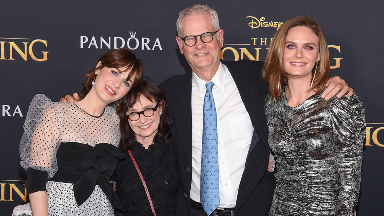 Emily Deschanel wears a silver dress and smiles next to her parents and sister on a red carpet