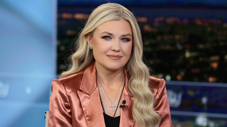 Erika Kirk smiling in a shiny orange blazer during a TV interview