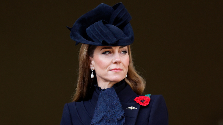 Kate Middleton looking thoughtful in a navy blue dress and matching hat