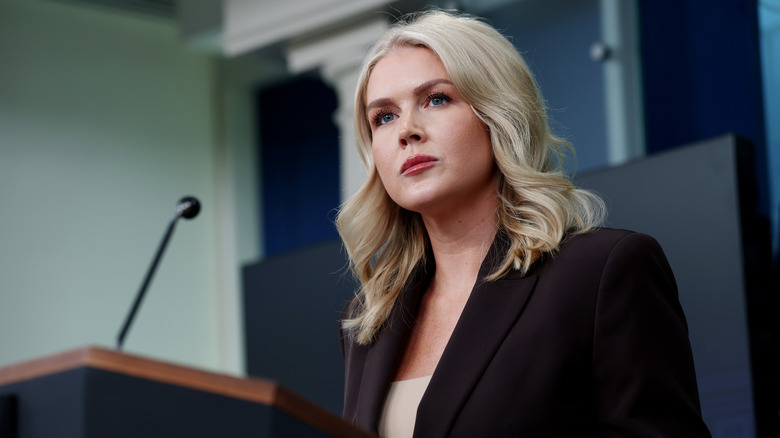Karoline Leavitt giving a press briefing in a black blazer with a white shirt underneath