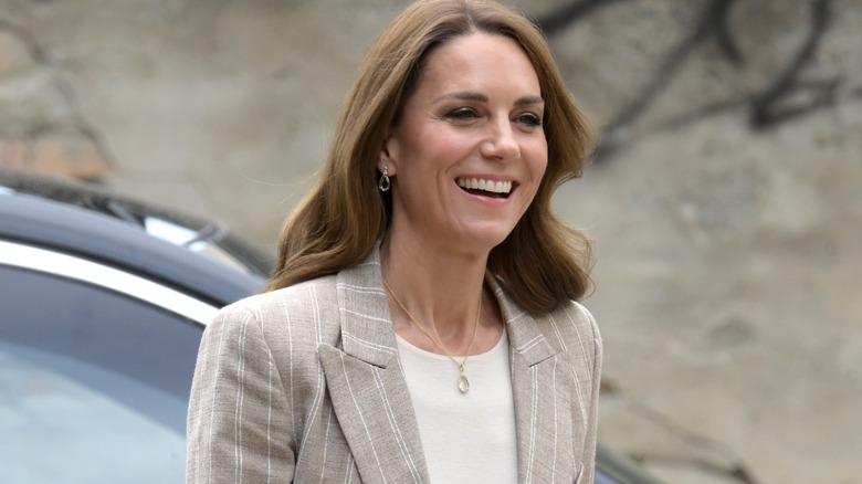 Princess Catherine laughing in a stripy tan blazer with her hair in loose waves