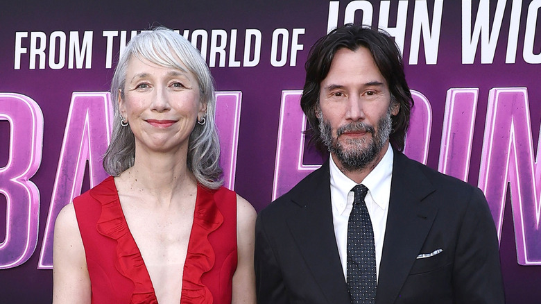 Alexandra Grant in V-neck red dress with Keanu Reeves in a white shirt and black tie and blazer