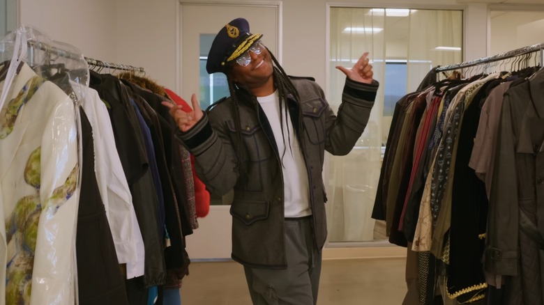 Law Roach posing between two clothes rails of his archive collection, smiling