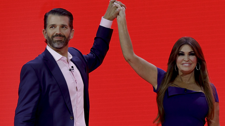 Donald Trump Jr. and Kimberly Guilfoyle hold hands with arms raised, smiling