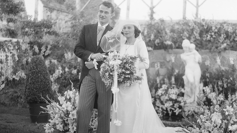 John Wayne in a suit standing next to Josephine Sáenz in a wedding dress