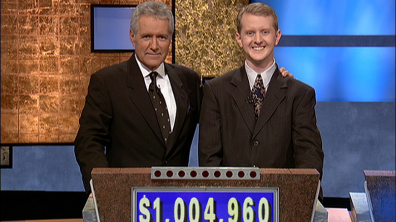 Jeopardy! host Alex Trebek posing with his arm around contestant Ken Jennings behind a podium.