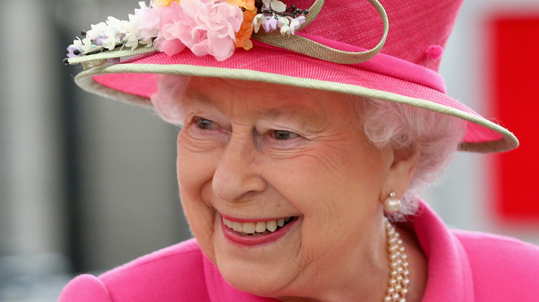 Queen Elizabeth smiles in a pink hat