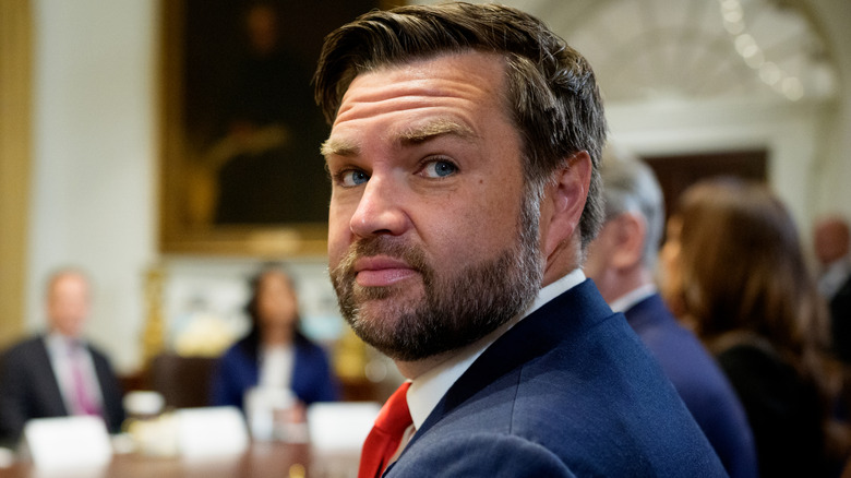JD Vance raising an eyebrow as he looks over his shoulder in a suit and red tie