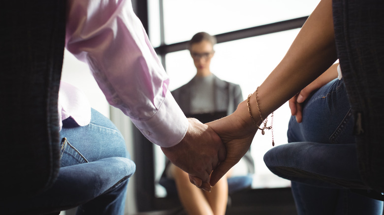 couple holding hands in foreground with marriage therapist in background