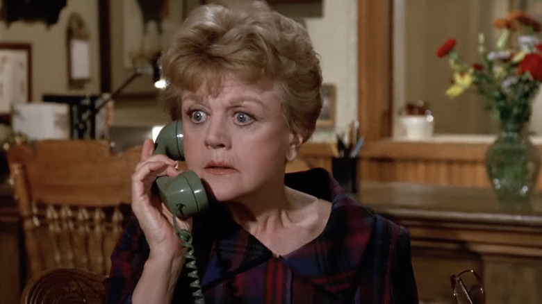 Angela lansbury holds green telephone to her ear, wears a plaid blouse