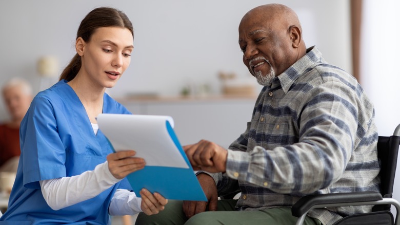 Medical clinic worker helping elderly patient in wheelchair with paperwork