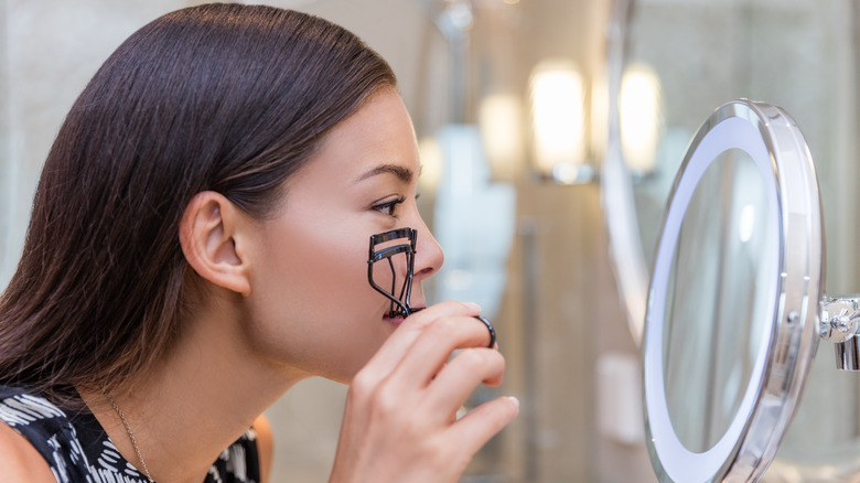 Asian woman curling eyelashes in front of mirror