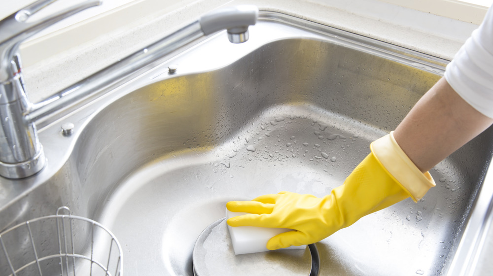 Woman with yellow gloves cleaning a kitchen sink