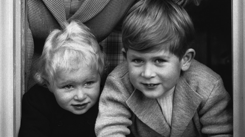 Princess Anne and King Charles as babies peeking out of a window 