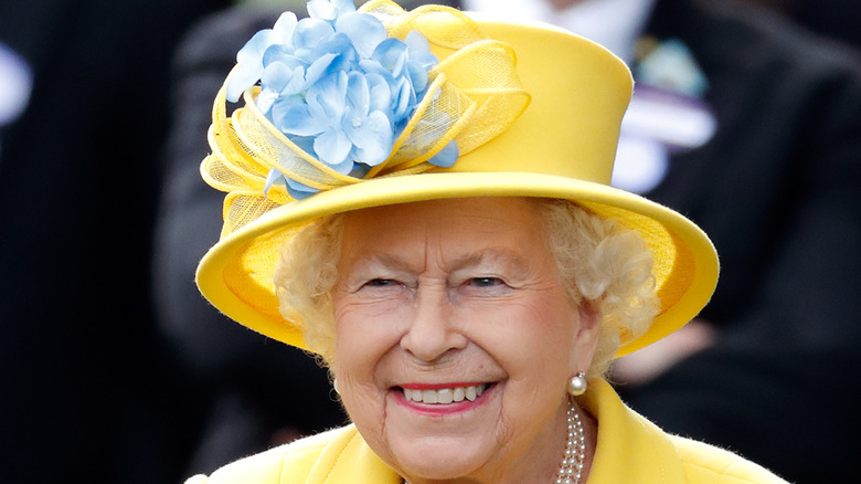 Queen Elizabeth smiling and wearing a yellow hat