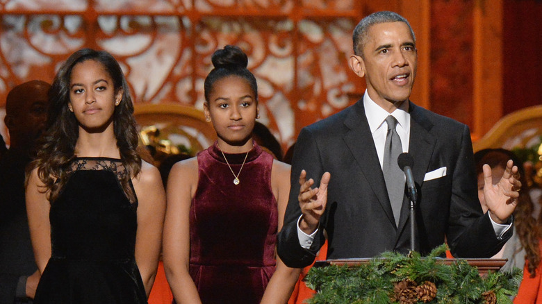 Barack Obama speaking while Malia and Sasha Obama stand behind him looking serious