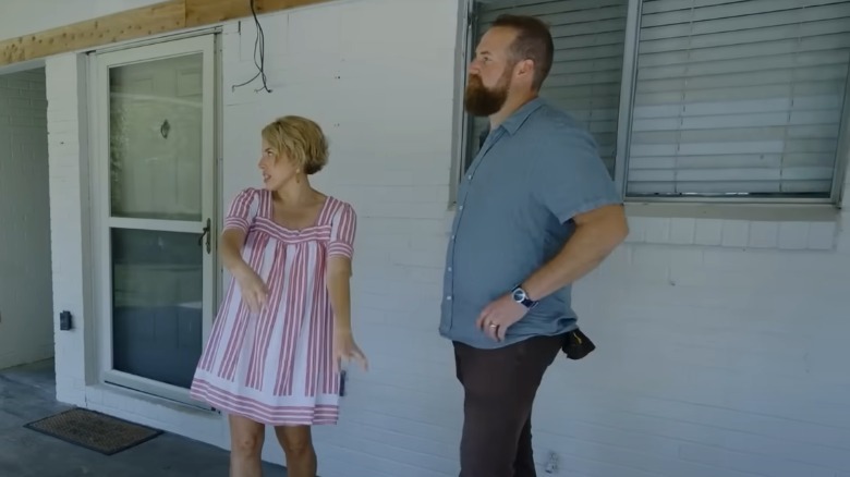 Erin Napier speaking and holding her arms out in 'Home Town' while Ben Napier stands with his hand on his hip