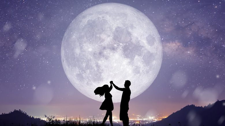 People dancing in front of a full moon. 