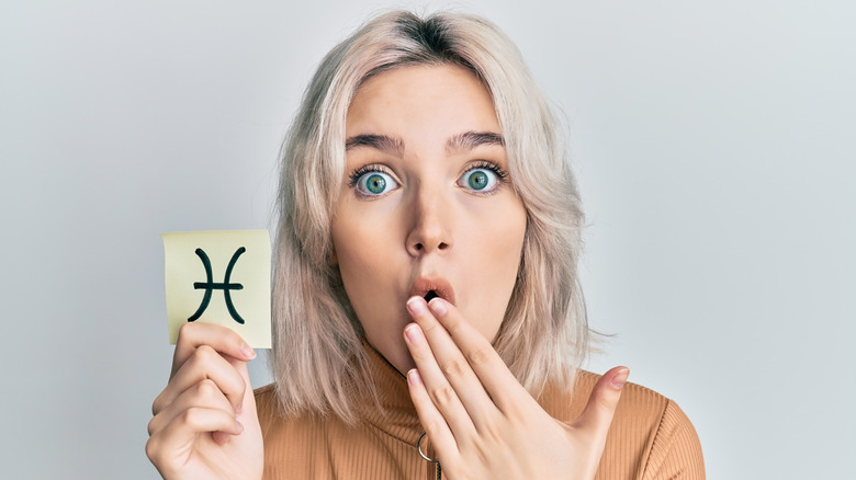 A woman holding a card with a Pisces sign on it.