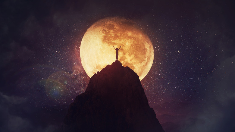 Person standing on mountain in front of full moon 