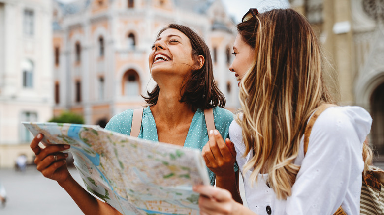 two women laughing and smiling while holding a map